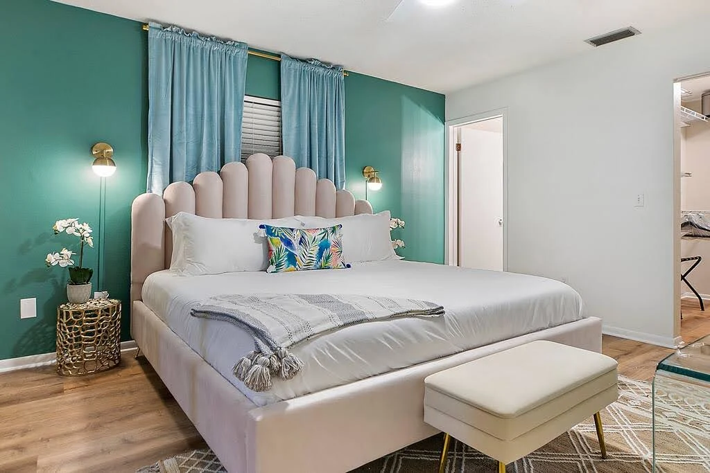 Airbnb bedroom with a teal accent wall, channel-tufted bed, and colorful pillows