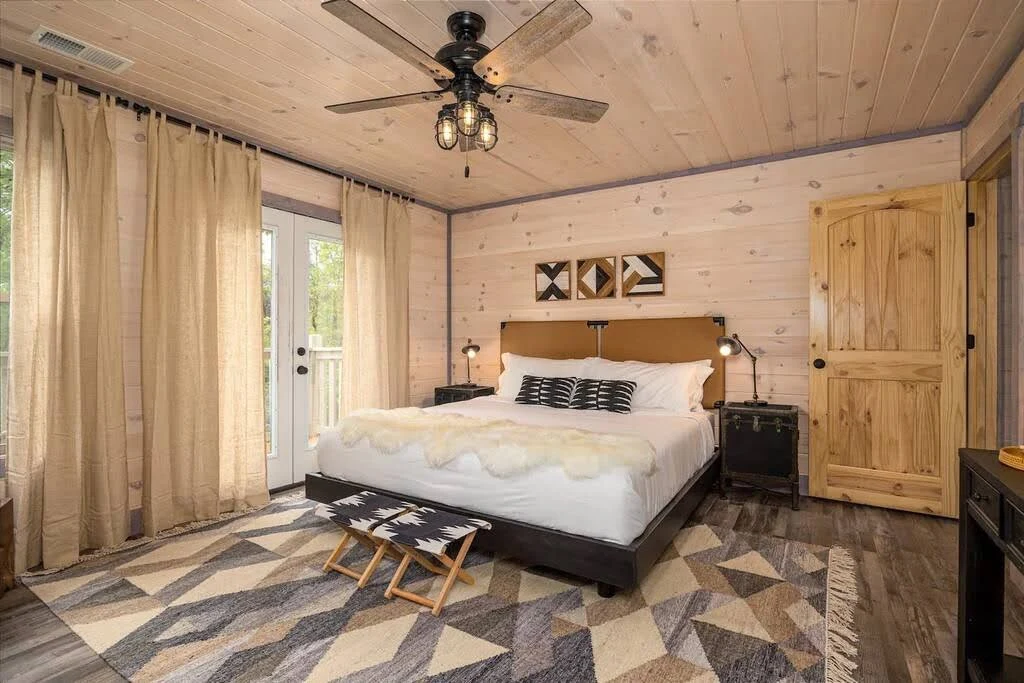 Rustic Airbnb bedroom with exposed beams, layered rugs, and warm neutral bedding