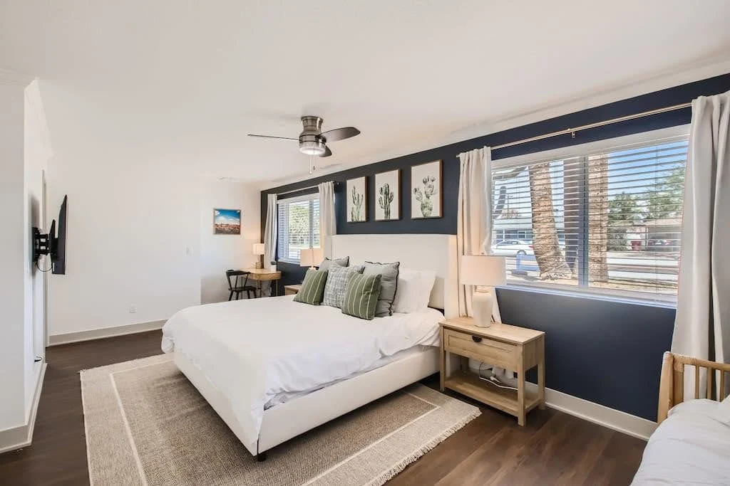 Desert Airbnb bedroom with sand-colored textiles, dark accents, and wide windows
