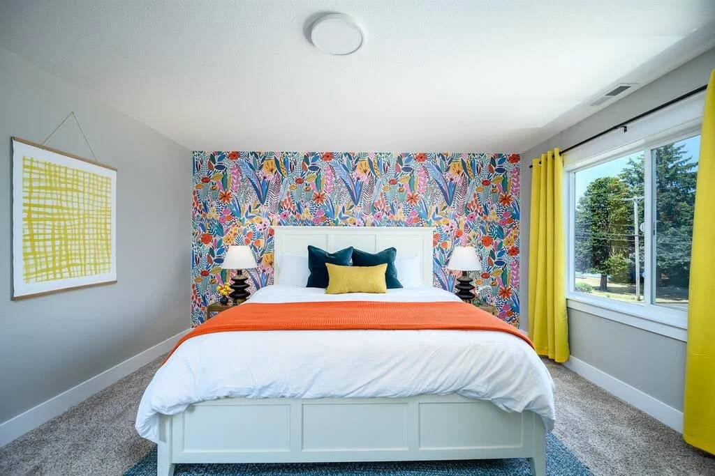 White Airbnb bedroom with colorful wall art, orange bedside tables, and green curtains