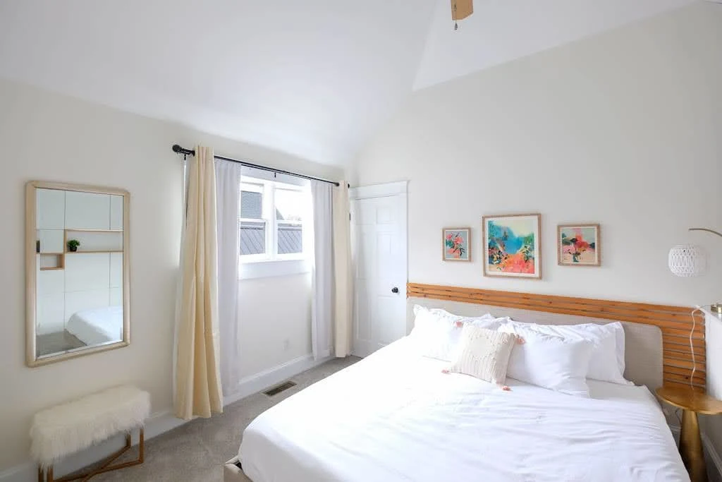 Bright seaside Airbnb bedroom with white bedding, pale blue walls, and small artwork